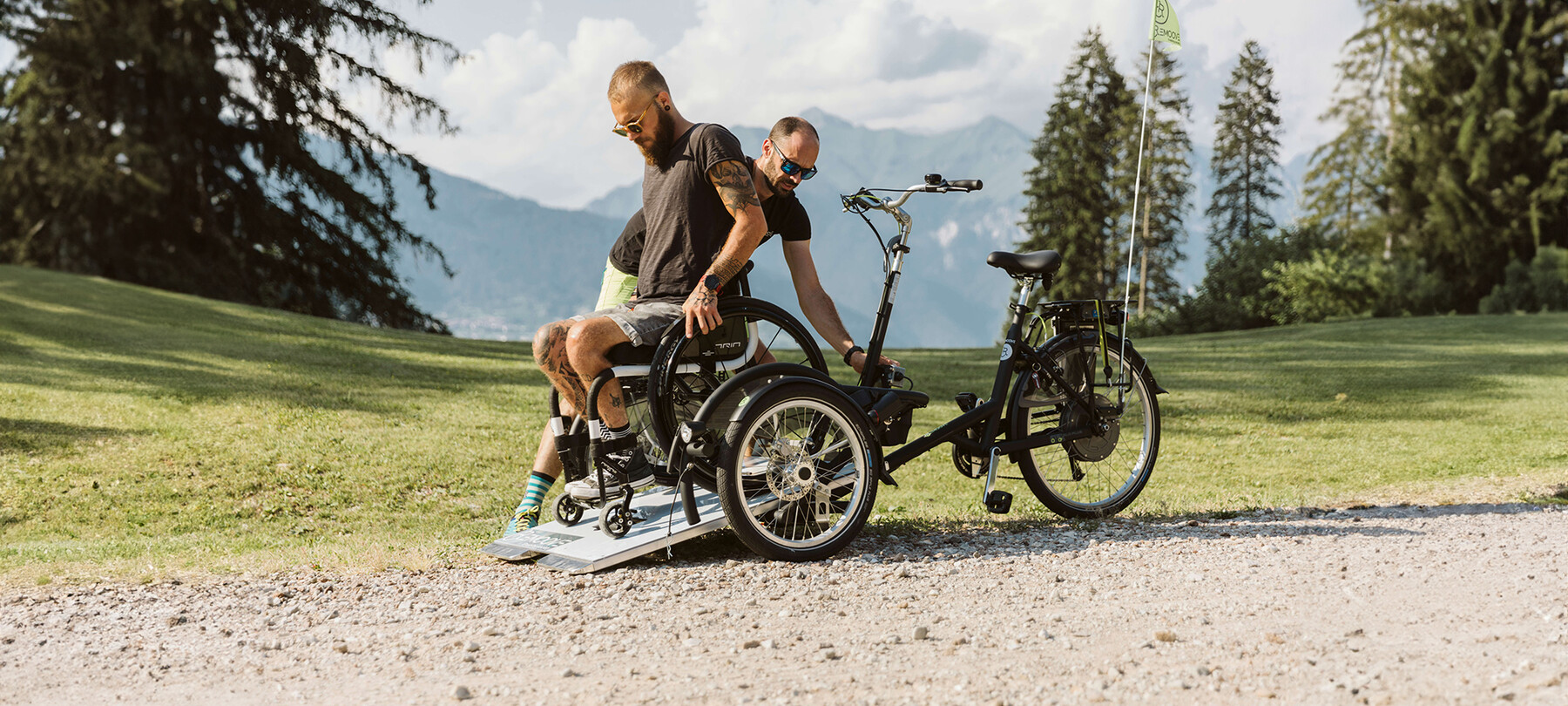 Un ragazzo in sedia a rotelle ha appena raggiunto la sede del concerto e sta scendendo dalla wheelchair bike con cui ha percorso il sentiero che dal parcheggio porta alla location. Una persona del team Remoove lo aiuta e si assicura che tutto avvenga in sicurezza.