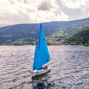 Un’imbarcazione a vela della Cooperativa Arché attraversa il lago di Caldonazzo. È una deriva accessibile adatta anche a persone con disabilità motorie. Non ci sono altre barche nel lago e l’immagine trasmette una sensazione di calma e silenzio. | © ©Trentino Marketing_Gianluca Prati_Accessibilita_Lago di Caldonazzo_2024_00005
