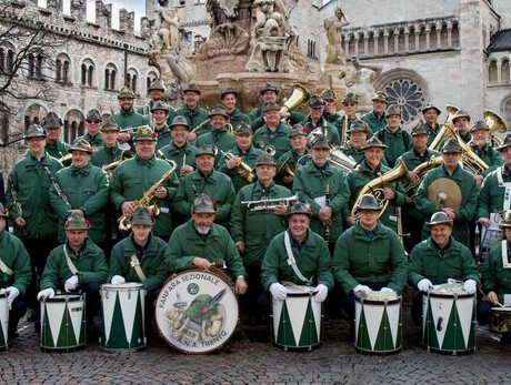 L'immagine mostra i componenti della Fanfara sezione ANA di Trento in posa sotto la fontana del Nettuno, in piazza Duomo a Trento