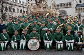 L'immagine mostra i componenti della Fanfara sezione ANA di Trento in posa sotto la fontana del Nettuno, in piazza Duomo a Trento