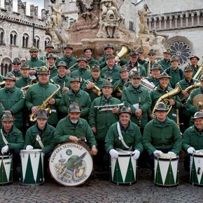L'immagine mostra i componenti della Fanfara sezione ANA di Trento in posa sotto la fontana del Nettuno, in piazza Duomo a Trento