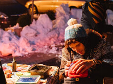 La foto ritrae un artista pitturare il viso ad un bambino per l'occasione natalizia
