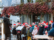 L'immagine mostra un coro di bambini vestito di rosso che cantano insieme melodie natalizie