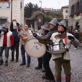 Nell'immagine si vedono i 5 componenti della banda intenti a suonare i loro strumenti in una piazza 
