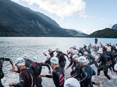 A group of X-Terra participants wearing wetsuits and swimming caps dive into Lake Molveno 