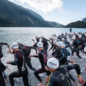 A group of X-Terra participants wearing wetsuits and swimming caps dive into Lake Molveno 