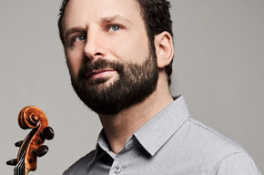 A man with a dark beard and micro-patterned gray shirt looks up towards the right against a gray background. At the bottom left, the neck and scroll of a violin are held near him.