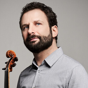 A man with a dark beard and micro-patterned gray shirt looks up towards the right against a gray background. At the bottom left, the neck and scroll of a violin are held near him.