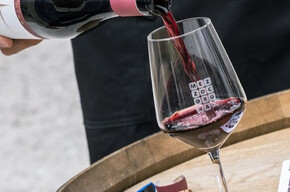 The image shows a bottle of Teroldego Rotaliano in the foreground being poured into a glass placed on a wooden barrel. Most likely, the bottle is being poured by a sommelier attending the event.