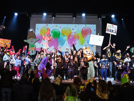 Nella foto sono presenti moltissime persone - adulti e bambini - vestiti in maschera mentre festeggiano il Carnevale al palacongressi di Andalo