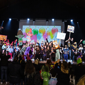 Nella foto sono presenti moltissime persone - adulti e bambini - vestiti in maschera mentre festeggiano il Carnevale al palacongressi di Andalo