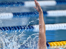 dynamic close-up of an athlete competing in the backstroke during an ice swimming championship. The arm is extended out of the water, creating a splash, as the athlete moves with determination in the pool lane.
