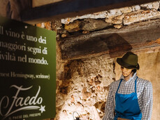 On the left, in the foreground and slightly in shadow, there is a sign that reads: 'Wine is one of the greatest signs of civilization in the world.' In the background, on the right, there is a statue of a craftsman working with wood, part of the life-sized nativity scene.