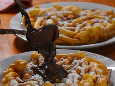 In the image, there is a close-up of the typical Trentino dessert ‘Strauben’, made from a fried batter. It is topped with powdered sugar and Nutella.