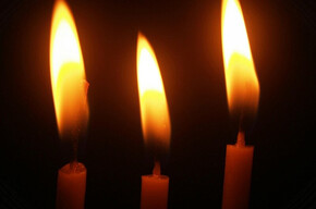 Tre candele accese su sfondo nero, con fiamme alte e luminose che brillano nell'oscurità.