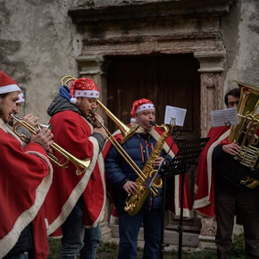 L'immagine ritrae 4 uomini vestiti con cappello e mantello di Babbo Natale suonano trombe e tromboni intonando canti natalizi