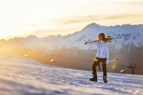 Woman carrying skis on shoulder in snowy mountain at sunset