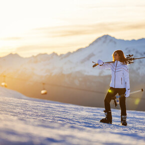 Woman carrying skis on shoulder in snowy mountain at sunset