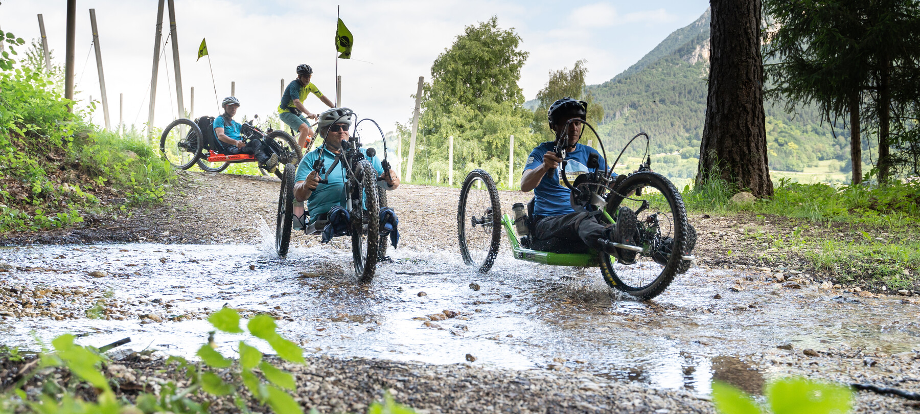 Siamo sull’Altopiano della Vigolana. È una bella giornata estiva, luminosa. Quattro turisti, amanti dell’attività outdoor, fanno biking seguendo un sentiero sterrato: tre di loro guidano una handbike. Insieme, si godono il sole sulla pelle, l’aria fresca e il verde dei boschi che li circonda. | © ©Trentino Marketing_Gianluca Prati_Accessibilita_Vigolana_2024_00012
